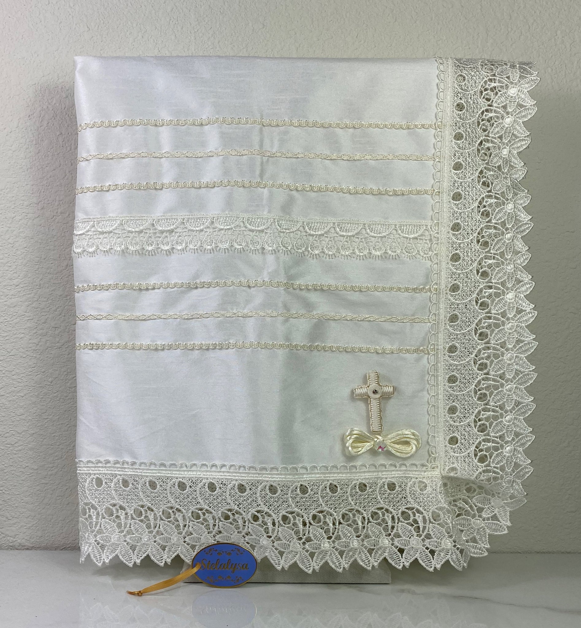 Beautiful ivory silk baptism blanket with an embroidered cross, elegant lace edge, bow, and jewels.