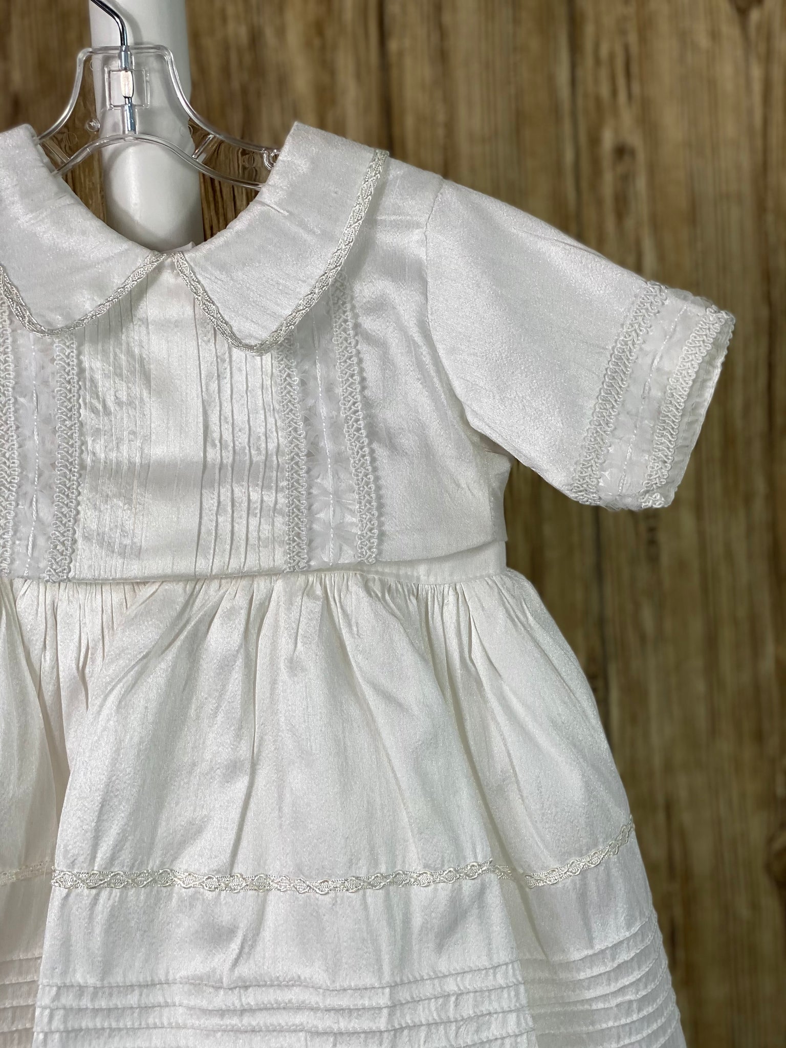 White, size 24M 2-piece set including romper and detachable over skirt Buttoning on cuffs Elastic banding on back of pants Collared with long sleeves Buttoning on back of romper and inside seam of legs Pinstriping layered on skirt, and on bodice of romper Mesh bowed trim layered on skirt, sleeve cuffs, and romper bodice Intricate swirled trim around mesh bowed trim