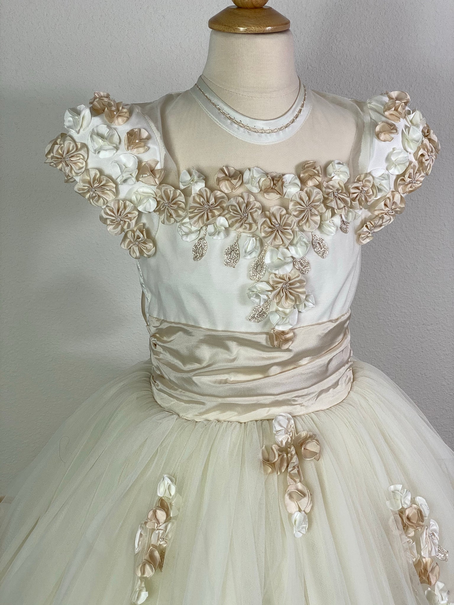 Ivory, size 8 Beige and Ivory floral covered cap sleeve Satin and mesh ivory illusion bodice with flower detailing Beige ruched cummerbund Layered tulle skirt lined with beige satin trim Floral cross detailing below bodice Satin covered button closure Beige ribboning for large bow