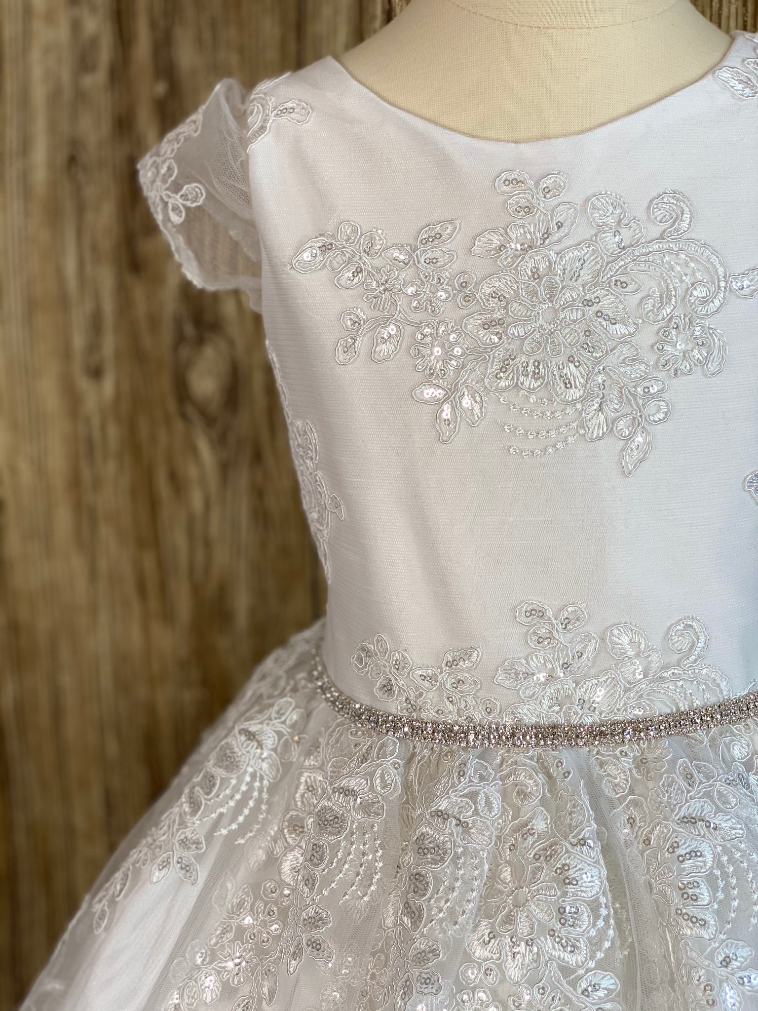 White, size 8 Lace cap sleeve Embroidered bodice with crystals throughout Rhinestone belt Satin skirt with embroidered tulle overlay and crystals Button closure Satin ribbon for bow