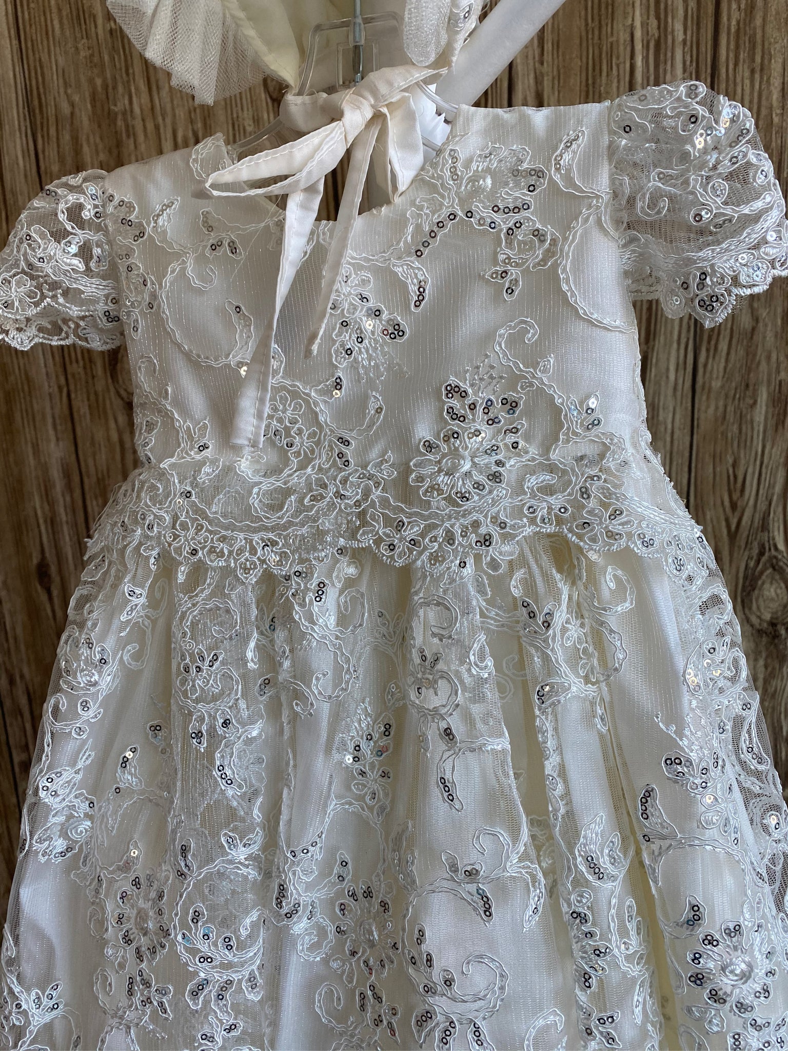 his a beautiful, one-of-a-kind baptism gown.  A lovely gown for a precious child.  Ivory, size 6M  Satin bodice with sequins embroidered lace overlay Sequins embroidered lace cap sleeve Pleated sequins embroidered lace skirting Satin bonnet with sequins embroidered lace overlay Tulle ruffled brim on bonnet