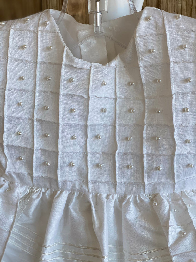 This a beautiful, one-of-a-kind baptism gown.  A lovely gown for a precious child.  White, size 6M Silk bodice with pleated square effect Pearls throughout bodice Two piece silk skirting Pleated square detailing on skirt with pearls throughout Ribboned pinstripes on skirting Ruffled trip along skirt edge Ruffled sleeves Button closure Matching bonnet
