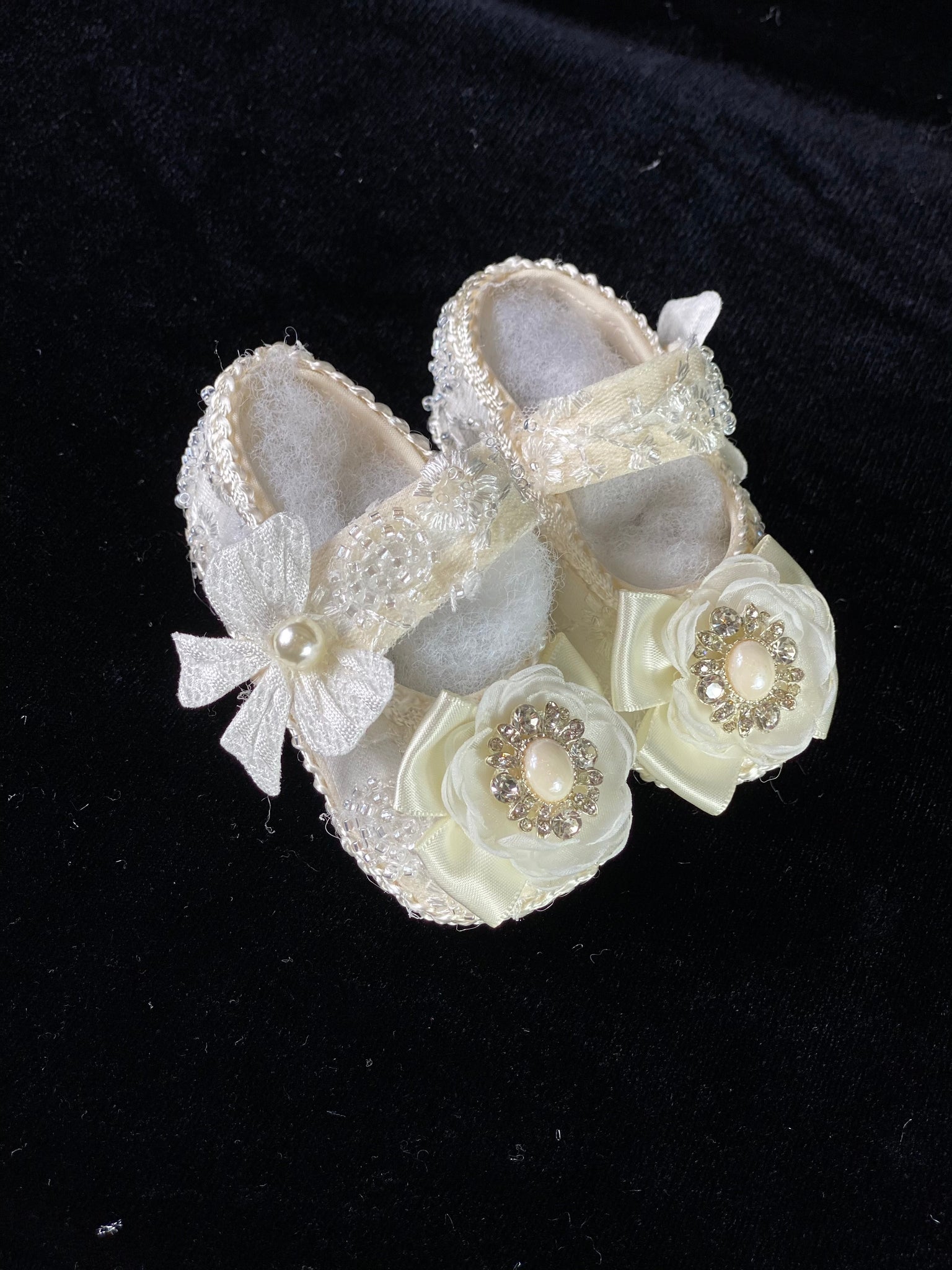 Elegant ivory handmade baby girl shoes with embroidery, lace, bows, flower, and jewels.