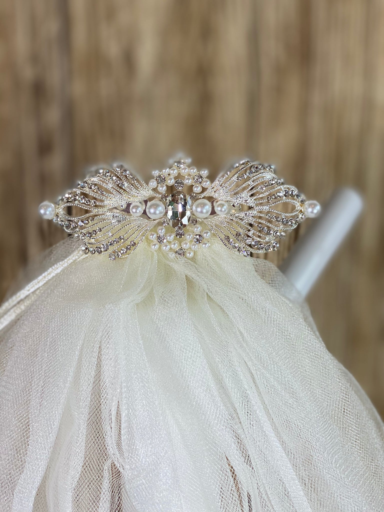 White - Elegant First Communion Veil on Decorative Comb  Elegant soft 2 layer tulle veil with delicate hand stitched braided satin trim around the edge and handmade decorative metal comb tiara with pearls and rhinestone detailing.  This double layered veil reaches approximately 21" long. Veil has 1.5" long, 2" wide, metal comb to secure it in place. 