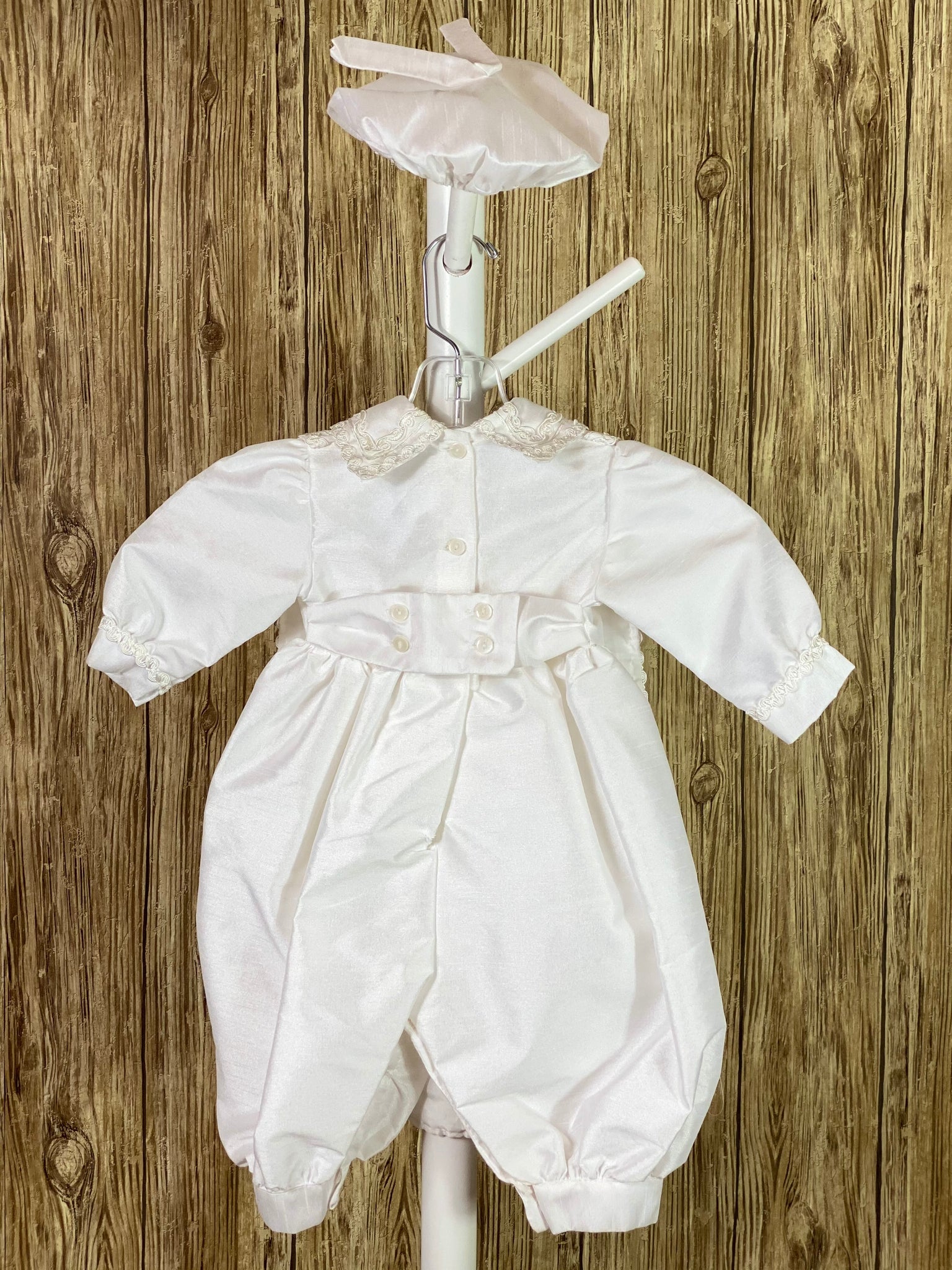 WHITE  3-piece white set including beret, one piece stole, romper Collared shirt with long sleeves Buttoning on pant cuffs Button closure on back of romper Wide embroidered trim along edge of stole and collar Thin embroidered trim along sleeve cuff edge Large pearl beaded cross on front of stole