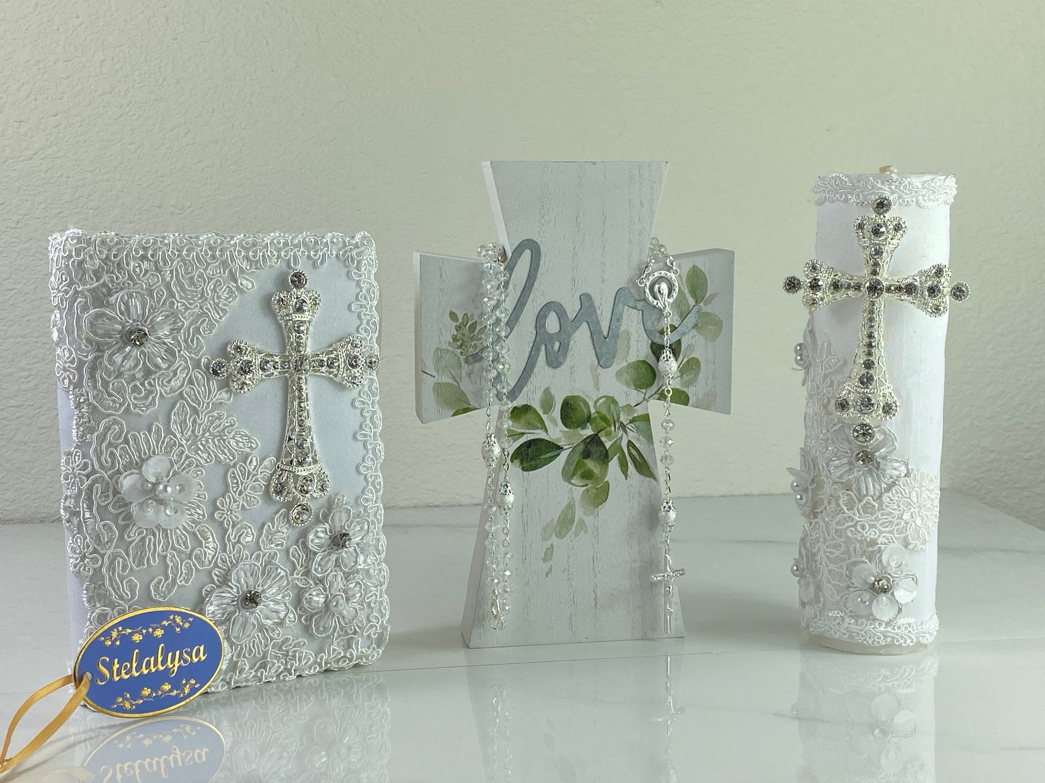This white Bible Set - candle and bible is handmade and made using satin.  It is elegantly designed with lace, rhinestones, and sequins.  Each piece has a beautiful cross.  The candle is cylinder in shape.  An elegant rosary complements this set.  The rosary is 16.5 in. long and Bible is 6.5 in. by 4.5 in. and the candles approximately the same height.  The Bible includes the Old and New Testament in English. 