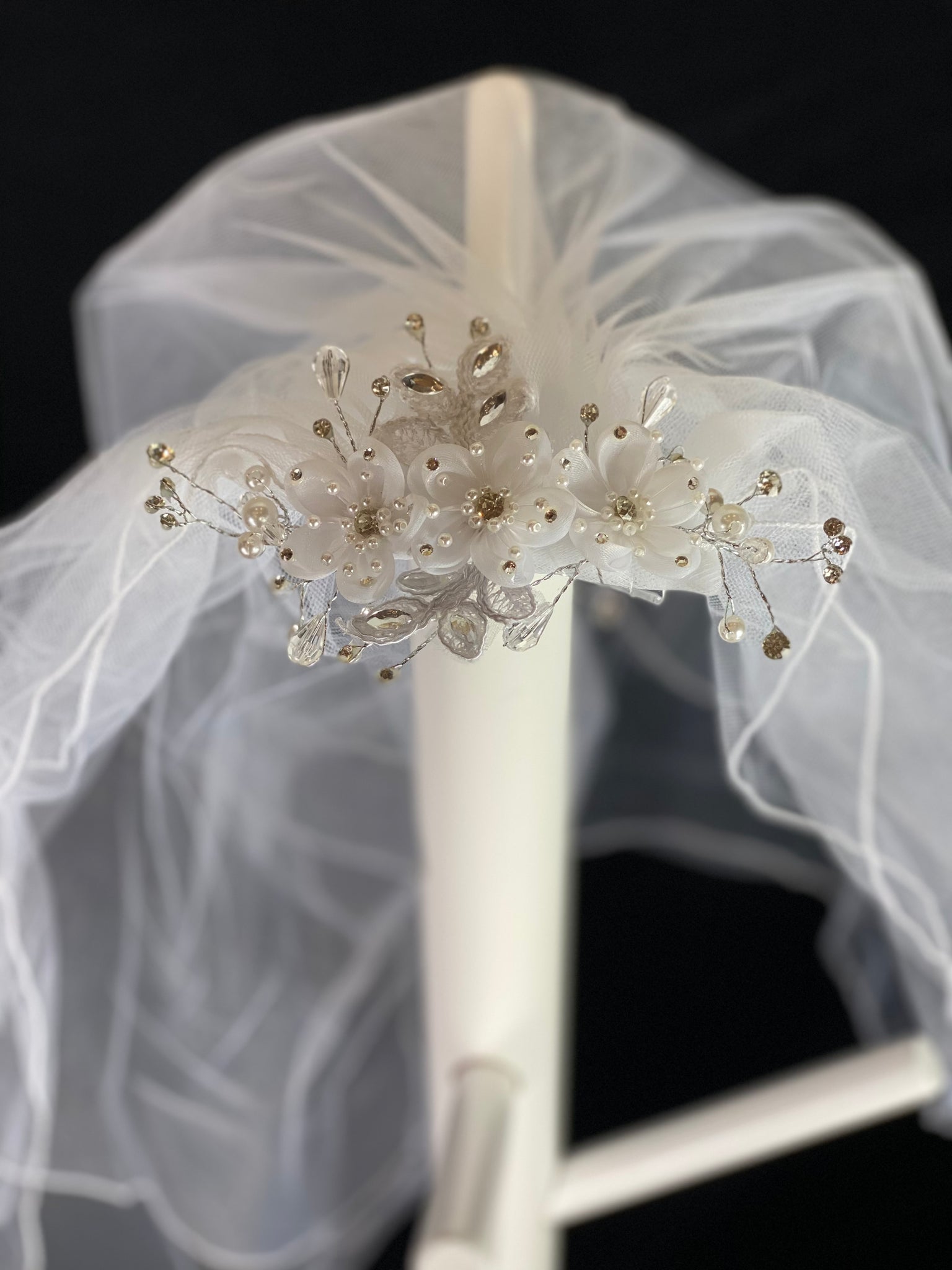 White Elegant Decorative Comb Veil with flowers and rhinestones.  Elegant soft 2 layer tulle veil with delicate hand stitched braided satin trim around the edge and handmade decorative comb with beautiful organza flowers through center with rhinestones on petals and centers. Stunning rhinestone leaves surrounding the flowers, with embroidered lace leaves through center flower.  This double layered veil reaches approximately 21" long. Veil has 2" long, 3" wide, comb to secure it in place. 