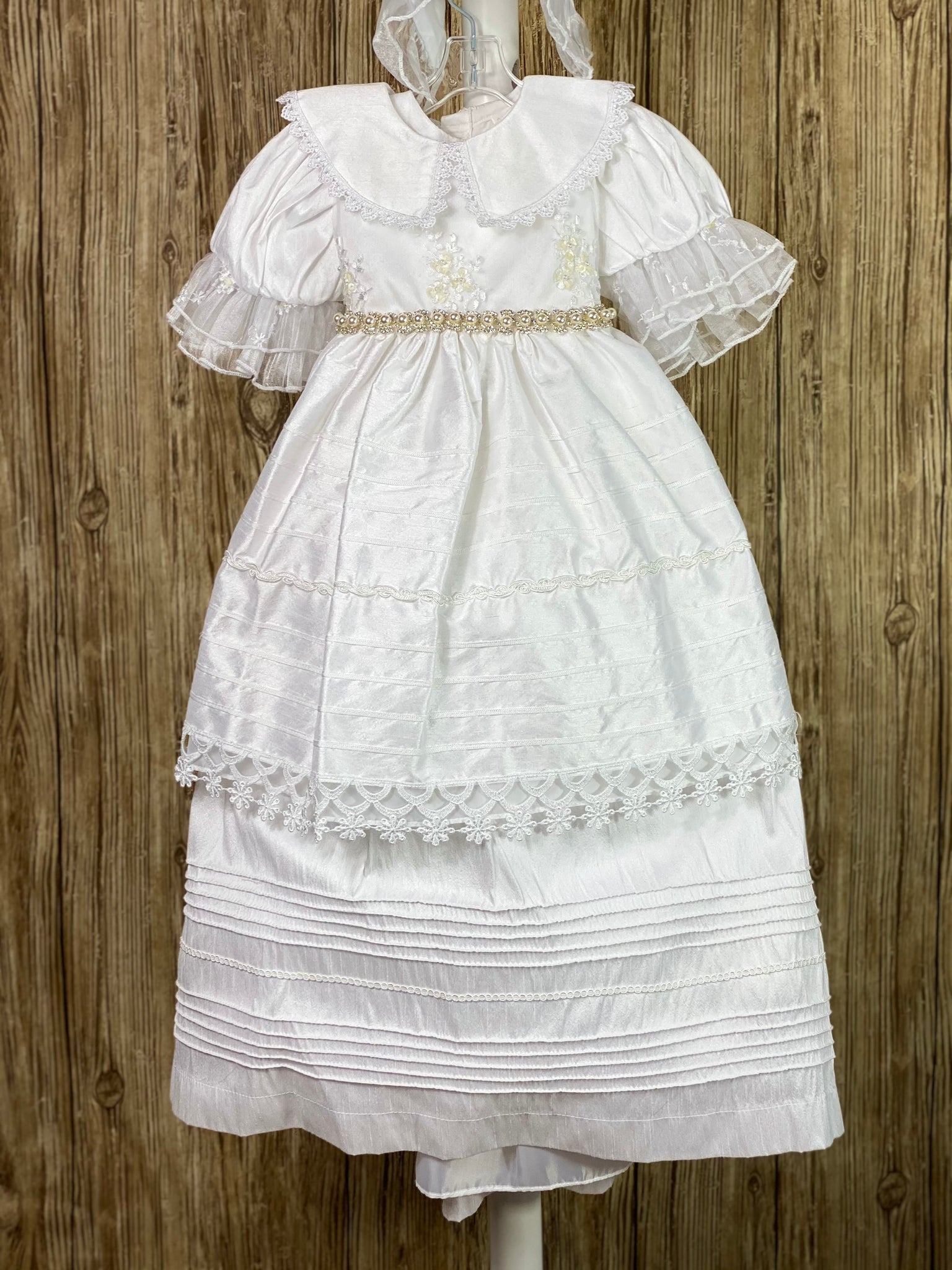 This a beautiful, one-of-a-kind baptism gown.  A lovely gown for a precious child.  White, size 12M Two layer dress Satin bodice with lace overlay Satin collar with lace trim Rhinestone pearl belting Puffed satin sleeves with lace trim Horizonal pinstripes with lace trim Second layer has horizonal pinstripes with lace trim  Satin bow in back Satin bonnet with ruffled lace brim