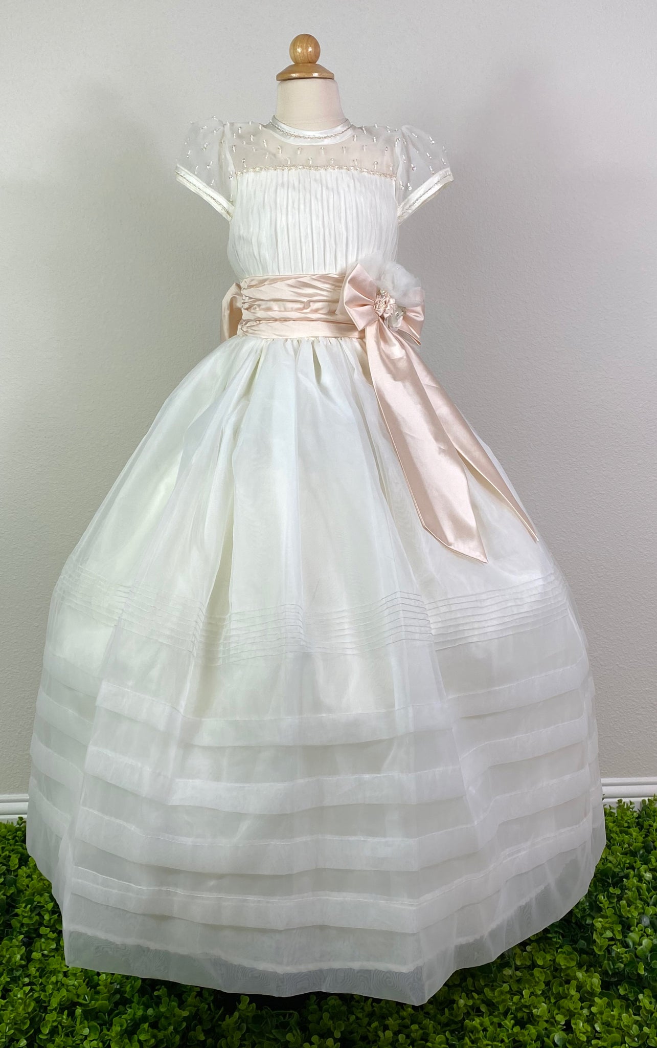 Ivory, size 10 Hand-stitched edging along sleeves and neckline Mesh and satin illusion bodice with beaded detailing and pleats Peach ruched cummerbund Large satin bow on front with floral detailing in center Meshed skirt with braided stripes along bottom Satin covered button closure Peach ribboning for large bow in back
