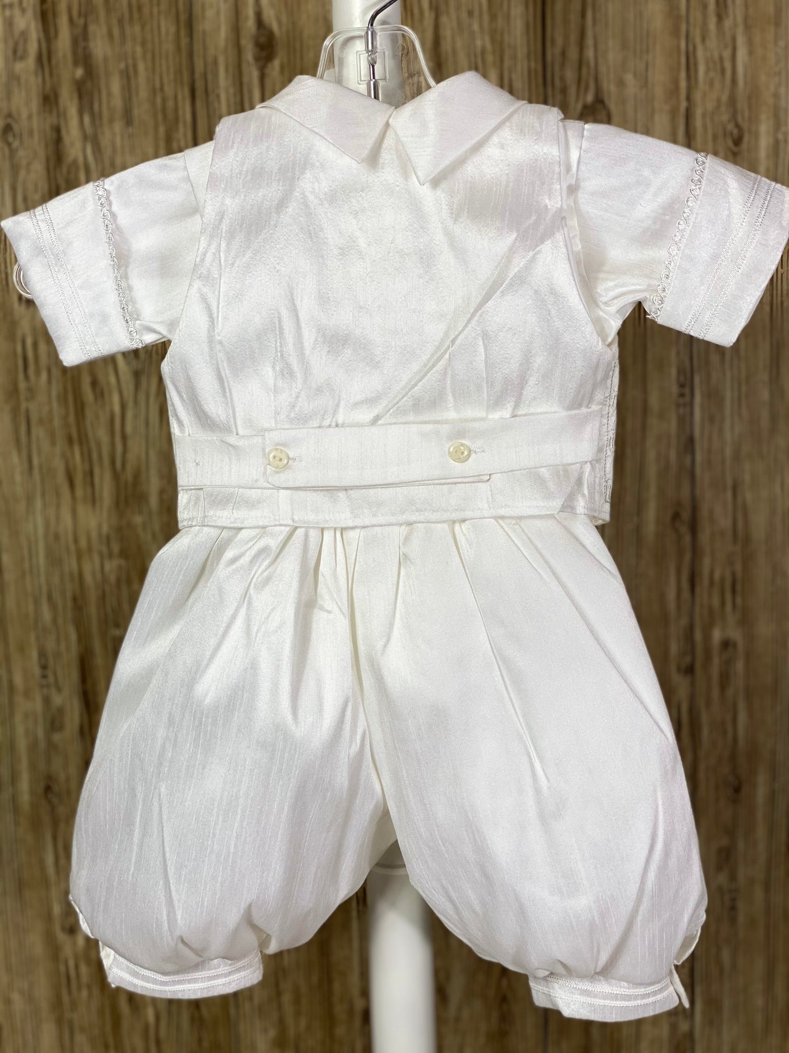 This a beautiful, one-of-a-kind boy’s baptism gown/set.  Lovely clothes for a precious child.   WHITE   4-piece white set including beret, vest, shirt, suspender pants JHS symbol embroidered into vest (JHS stands for Jesus Holmium Salvatore, Latin for Jesus Savior of Mankind) Tassel pin with 3 rhinestone centered circles Thin trim along cuffs, beret, and up pant legs Collared shirt with short sleeves Buttoning on pant cuffs Elastic banding behind pants Button closure on back of shirt
