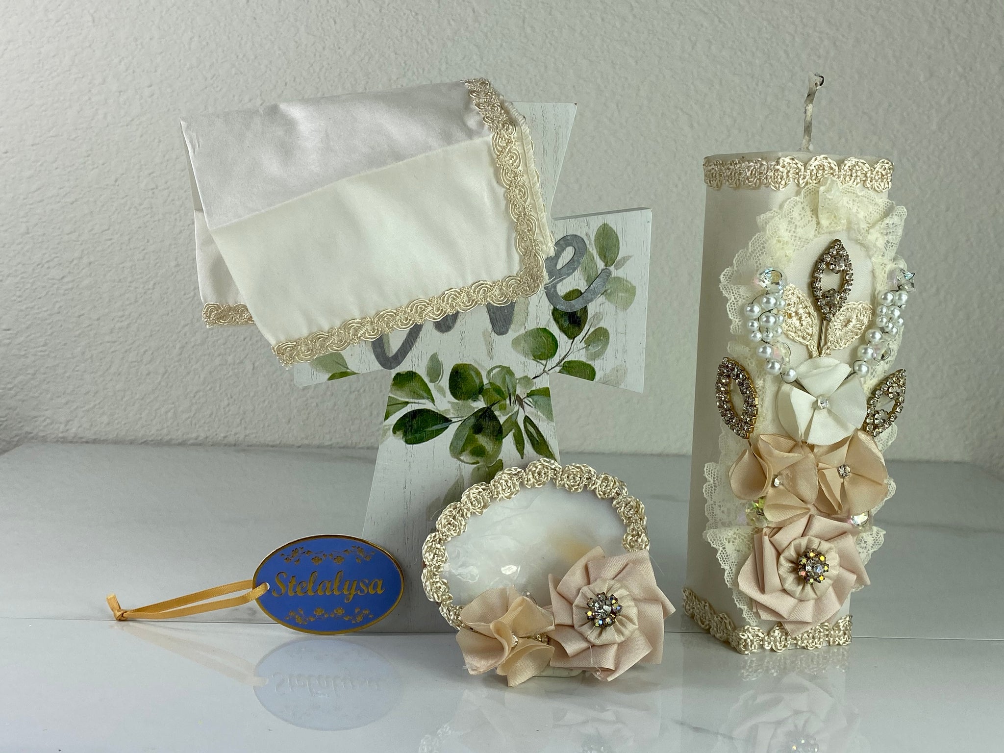 These one-of-a-kind Candle set is handmade and ivory in color.  This candle can also be use with a white baptism outfit because it has an array of light colors including white.   It is uniquely decorated with ribbon, pearls, crystals, flowers, and beads making it a gorgeous keepsake.   This candle is square in shape.    To match, the Shell is put together piece by piece to compliment the Candle and Handkerchief.  The Handkerchief is made of satin and embroidered lace 