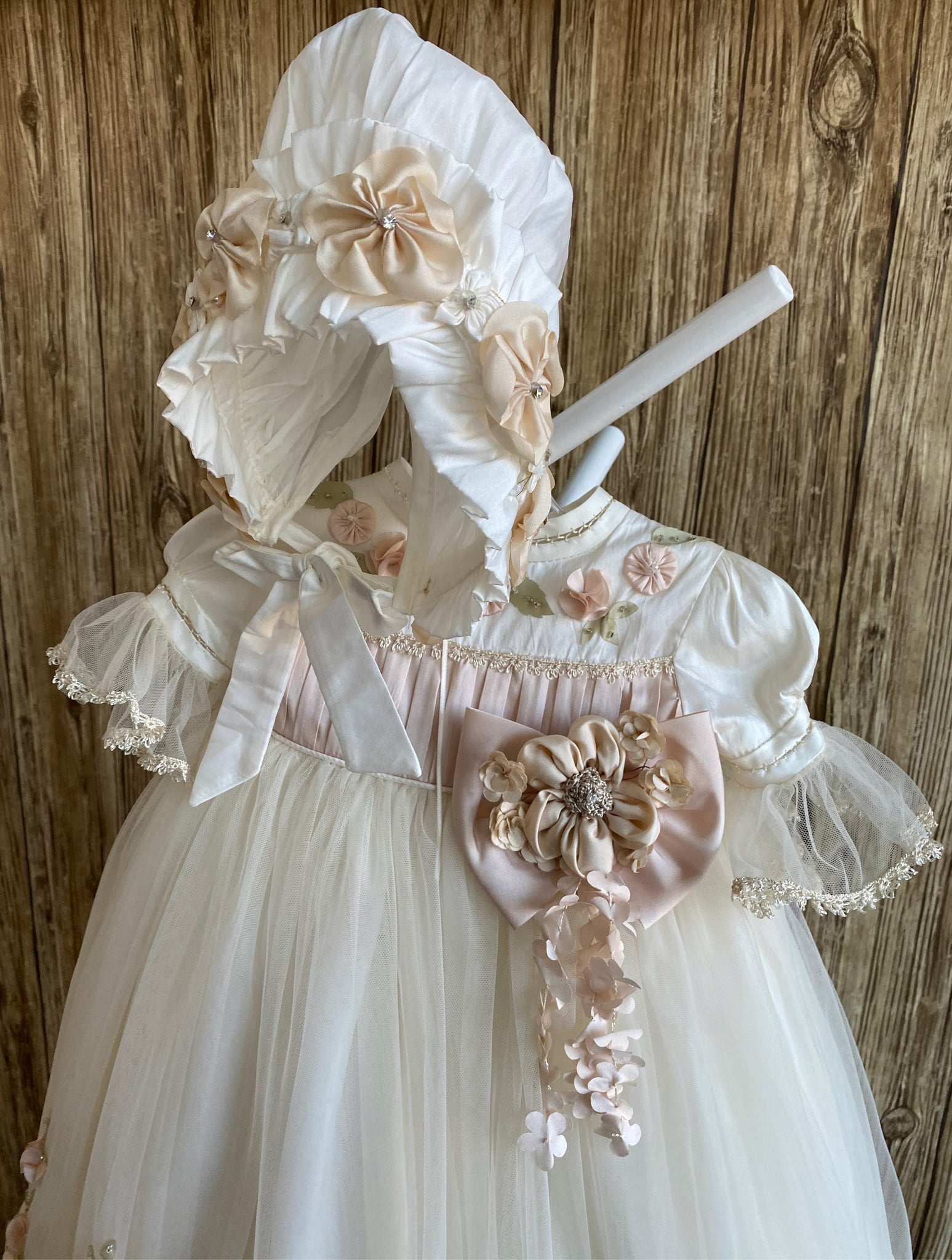 This a beautiful, one-of-a-kind baptism gown.  A lovely gown for a precious child.  Dress, Ivory, size 12M Satin bodice with dusty rose pleating  Organza flowers along bodice Satin puff sleeve with tulle brim Large dusty rose bow with Champaign flower center Tulle skirting with leaf detailing Dusty rose flowers along skirting bottom Slip  Satin bodice Layer one- satin with lace trim Layer two- embroidered lace Layer three- satin with dotted mesh overlay 