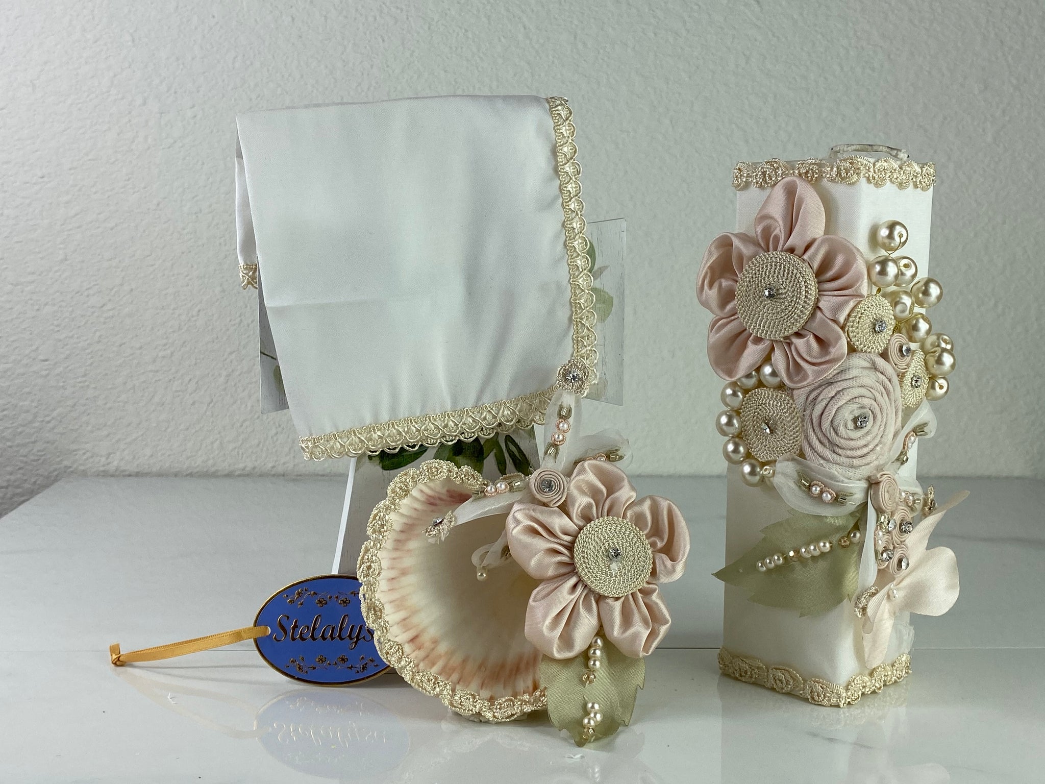 These one-of-a-kind Candle set is handmade and ivory in color.  This candle can also be use with a white baptism outfit because it has an array of light colors including white.   It is uniquely decorated with ribbon, pearls, crystals, flowers, and beads making it a gorgeous keepsake.   This candle is square in shape.    To match, the Shell is put together piece by piece to compliment the Candle and Handkerchief.  The Handkerchief is made of satin and embroidered lace 