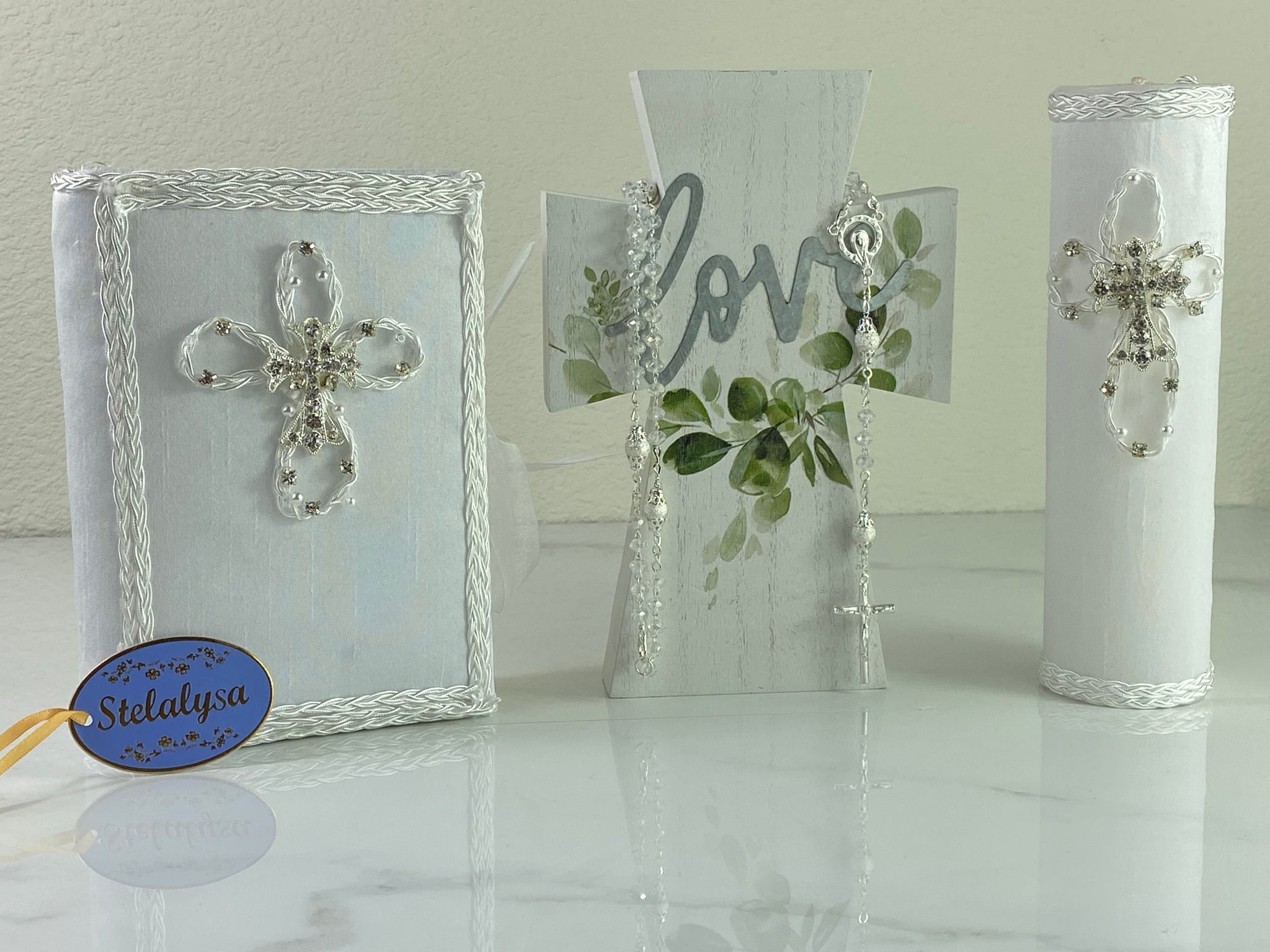 This white Bible Set - candle and bible is handmade and made using satin.  It is elegantly designed with lace and rhinestones.  Each piece has a beautiful cross.  The candle is cylinder in shape.  An elegant rosary complements this set.  The rosary is 16.5 in. long and Bible is 6.5 in. by 4.5 in. and the candles approximately the same height.  The Bible includes the Old and New Testament in English. 