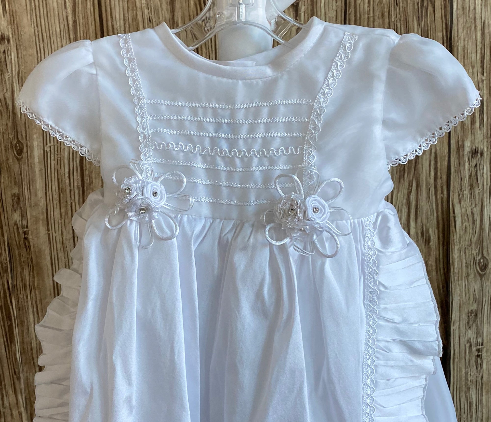 This a beautiful, one-of-a-kind baptism gown.  A lovely gown for a precious child.  White, size 12M Cropped satin bodice Embroidered detailing on bodice Two flowered bouquets on edging of bodice Satin cap sleeve with hand stitching along edge Long layered skirting Embroidered striping detailing on top layer of skirt Ruffled edge along skirt layers Satin bonnet with hand stitched edging Ribbon closure to tie around the head