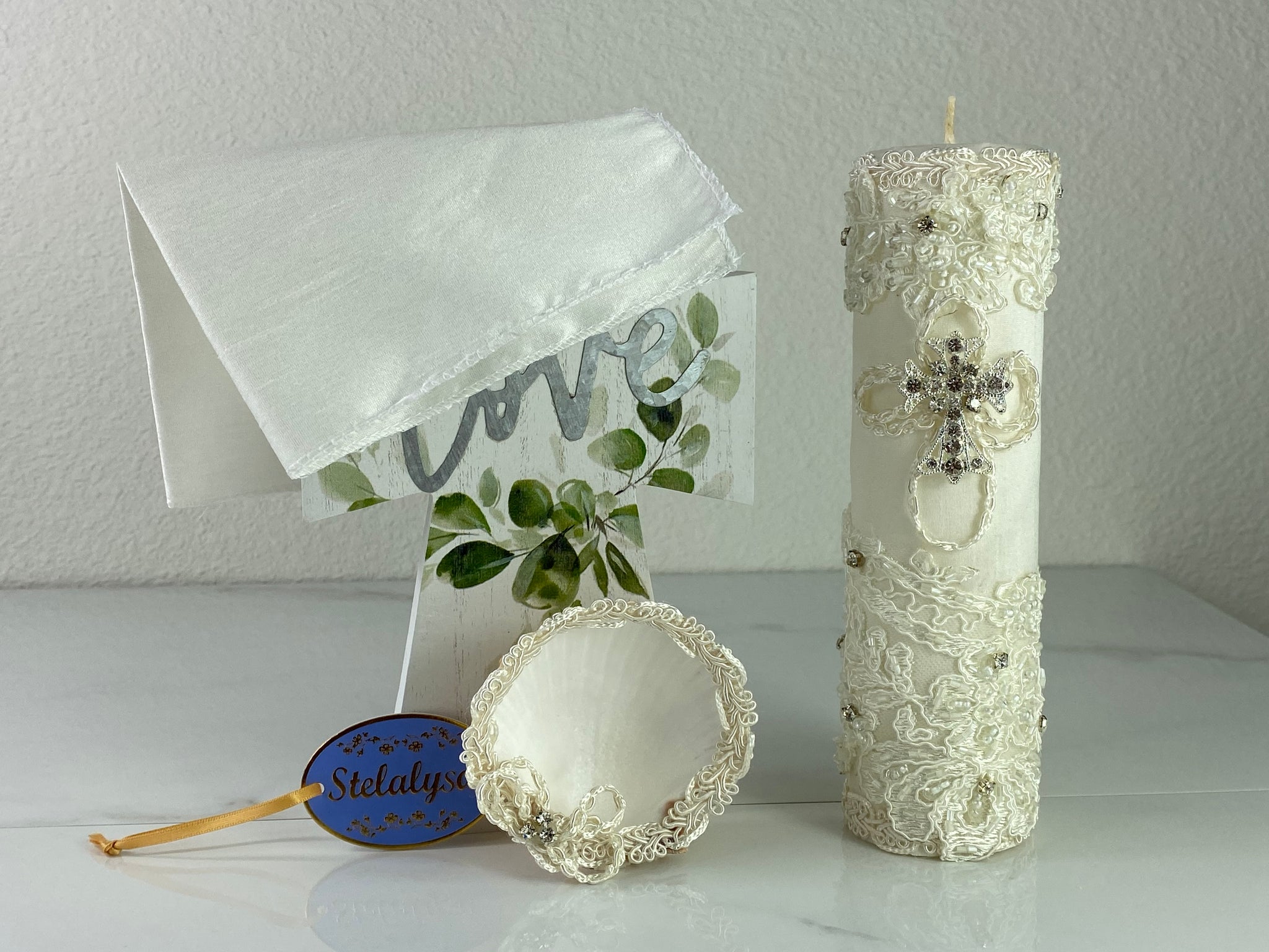 These one-of-a-kind Candle set is handmade and ivory in color.  This candle beautifully wrapped in lace.   It is decorated with a cross made of crystals making it a gorgeous keepsake.   This candle is cylinder in shape.    To match, the Shell is put together piece by piece to compliment the Candle and Handkerchief.  The Handkerchief is made of satin and embroidered lace to match the Shell and Candle beautifully.  