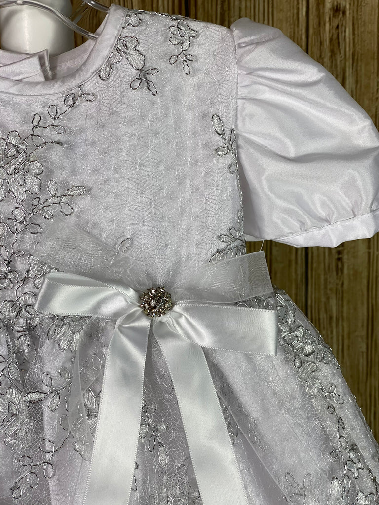 This a beautiful, one-of-a-kind baptism gown.  A lovely gown for a precious child.  White, size 24M Satin bodice with embroidered silver lace overlay Satin puffed sleeves Satin ribbon bow with rhinestone center Satin pleated skirting with embroidered silver lace layer Satin bow in back
